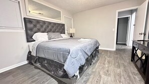 Un dormitorio con una cama grande, un aparador y una puerta que da a otra habitación.
