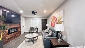 A living room with a flat-screen TV, a ceiling fan, a sofa, a coffee table, and a painting on the wall. - Cozy 2-Bedroom Peaceful Modern Home - Monthly Discount (Riverdale)