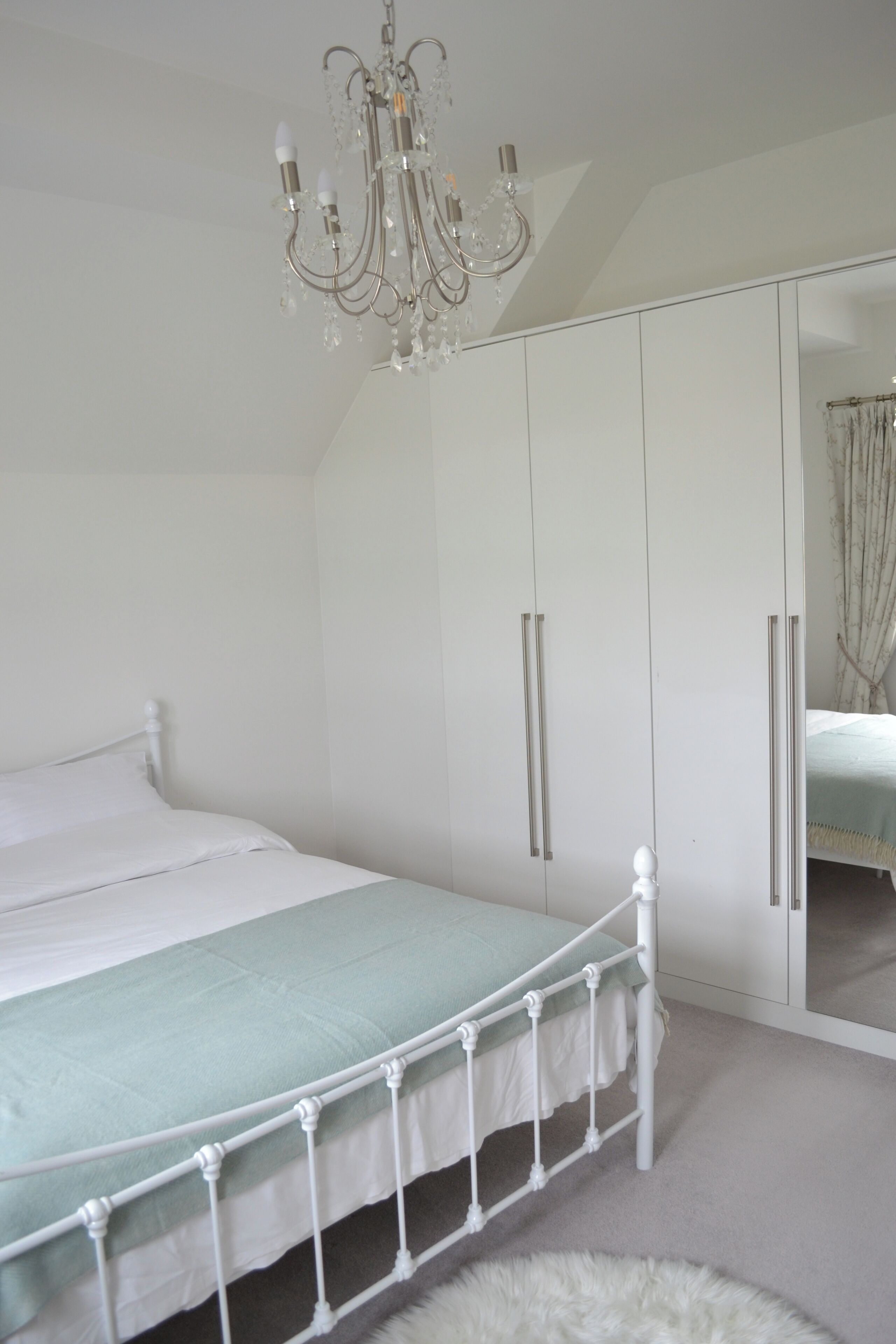 A bedroom with a bed, a white wardrobe, and a chandelier.