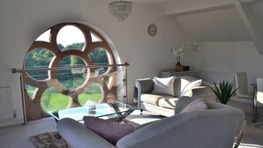 Una sala de estar moderna con un ventanal circular grande, una mesa de centro de vidrio, un sofá y una planta en maceta.