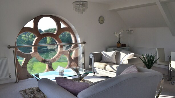 A modern living room with a large circular window, a glass coffee table, a sofa, and a potted plant. - The Residence, 3-bed Apt, Sleeps 6 With Parking (Lancaster)