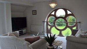 Una sala de estar moderna con un televisor grande, asientos cómodos, una mesa de centro de vidrio y una vista a través de una ventana peculiar.