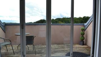 A covered patio area with a table and chairs, a small potted plant, and a view of a green landscape.