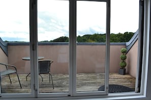 A covered patio area with a table and chairs, a small potted plant, and a view of a green landscape. - The Residence, 3-bed Apt, Sleeps 6 With Parking (Lancaster)