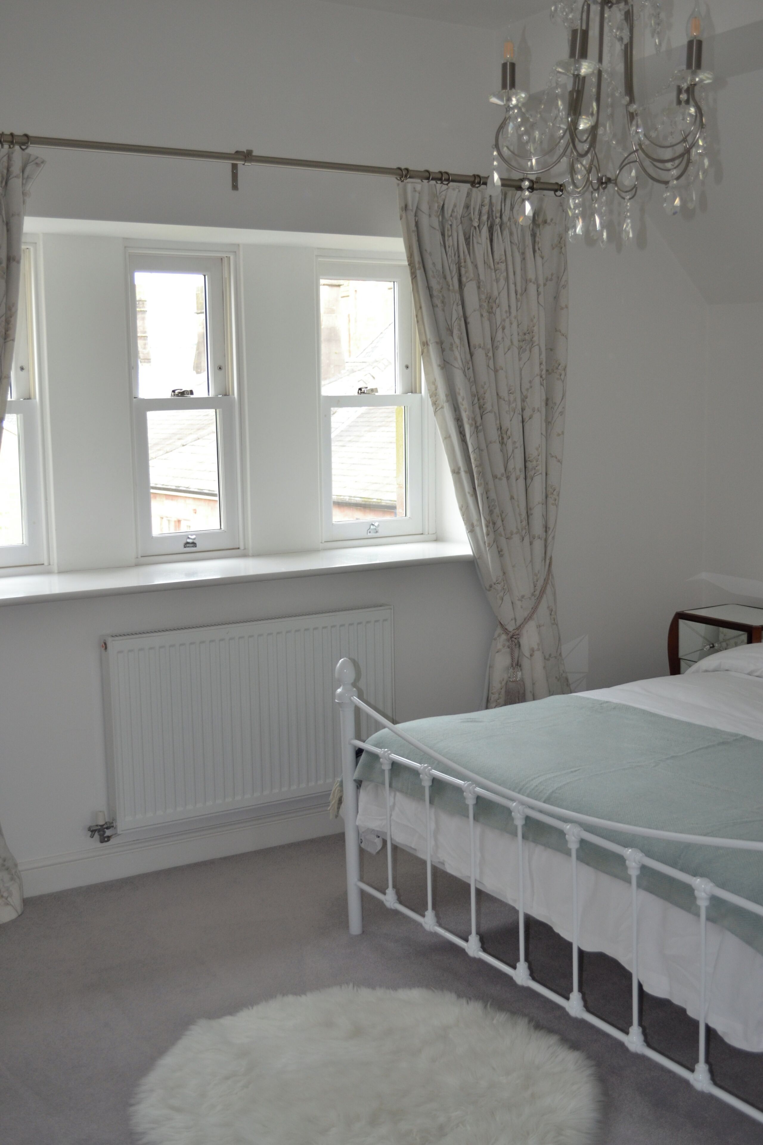 A bedroom with a bed, a radiator, a window with curtains, and a chandelier.