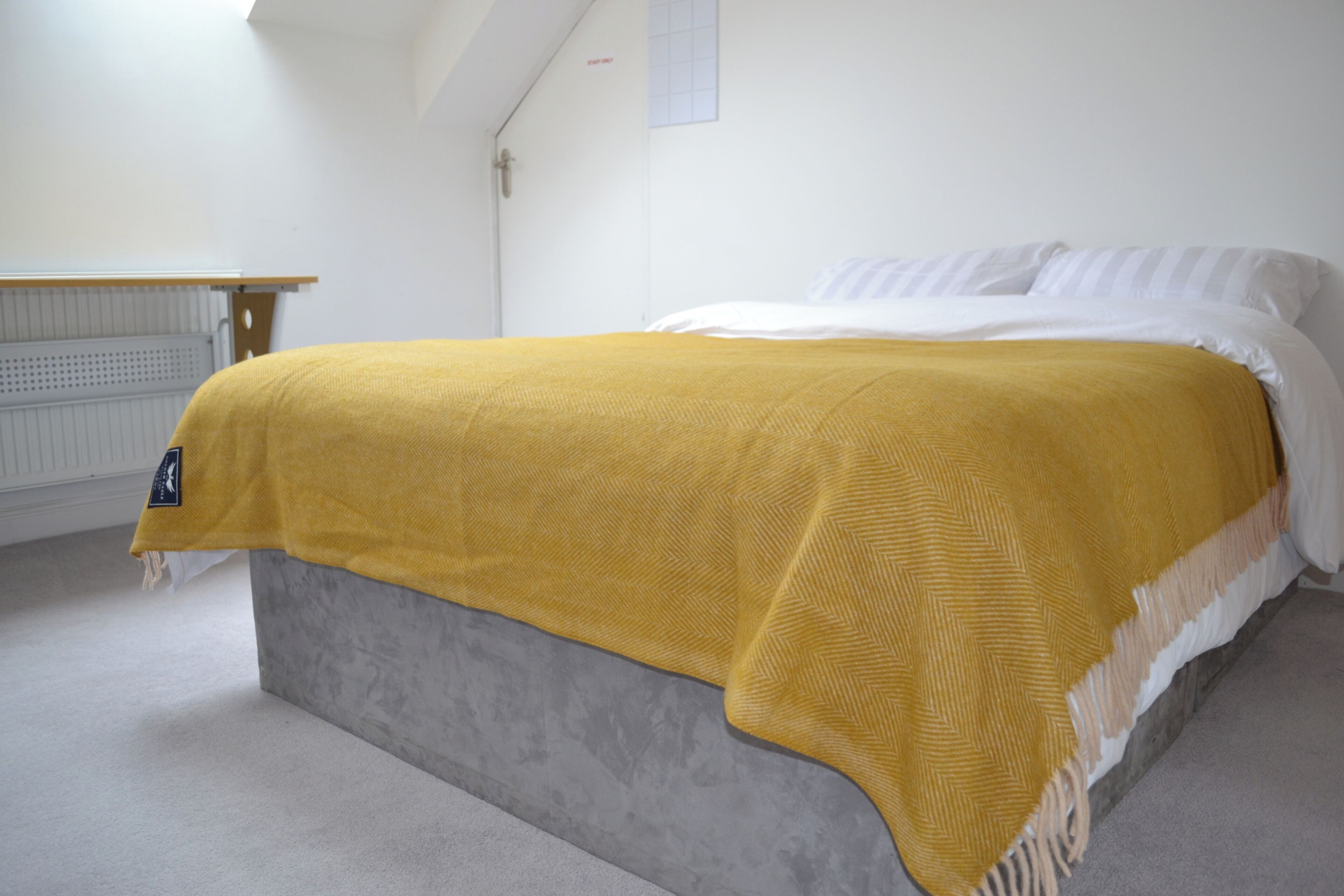 A bed with a grey headboard, a white mattress, and a mustard-colored blanket.