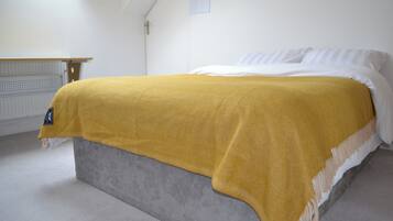 A bed with a grey headboard, a white mattress, and a mustard-colored blanket.