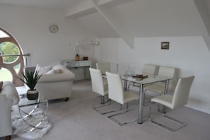 A modern, white-themed living room with a glass dining table and chairs, a sofa, a potted plant, and a clock on the wall. - The Residence, 3-bed Apt, Sleeps 6 With Parking (Lancaster)