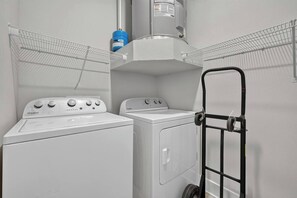 Una sala de bugaderia amb una rentadora i una màquina d'assecar roba Whirlpool, un escurapousses metàl·lic i un acumulador d'aigua.