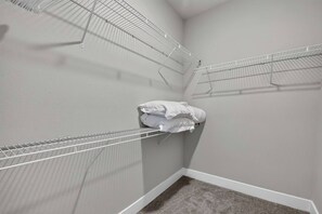 Habitació d'angle amb una catifes blanca, una paret blanca i una prestatgeria metàl·lica amb roba de llit blanca arremolinada.