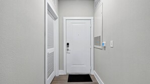 Ein schmaler Flur mit einer weißen Tür, einer schwarzen Fußmatte und einem an der Wand befestigten Thermostat.