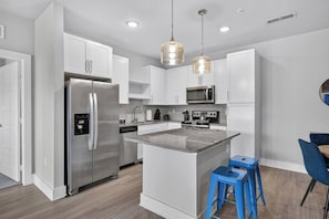 A modern kitchen with stainless steel appliances, white cabinetry, and a central island with stools. - Plush 2BR Apt/Pool/Gym/King Bed/Beachwalk access (St. Johns County)