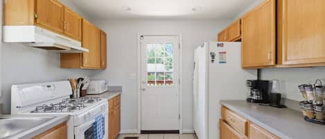A compact kitchen with wooden cabinets, a gas stove, a microwave, and a refrigerator.