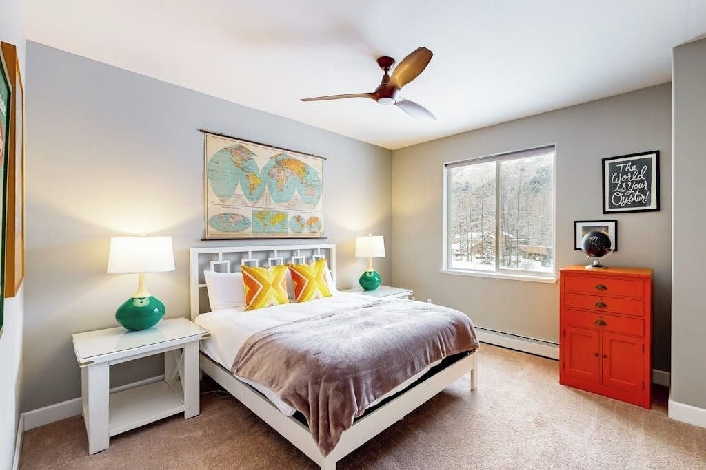 A bedroom with a bed, nightstands, a globe, a window, and a red dresser.