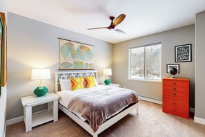 Une chambre à coucher avec un lit, des tables de chevet, un globe terrestre, une fenêtre et une commode rouge.