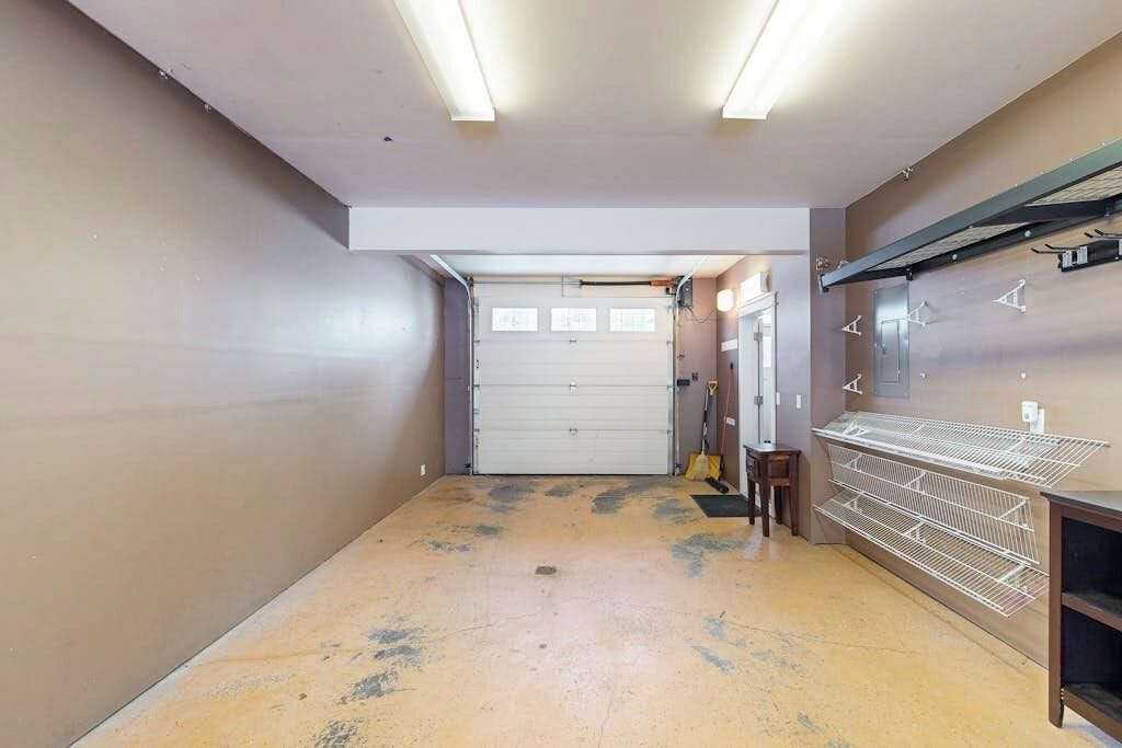 A hallway with a garage door, a broom, and a metal shelf unit.