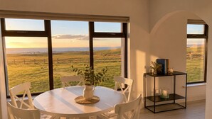 Comedor con una mesa redonda y sillas, un florero con flores y vistas a un campo verde a través de ventanas amplias.