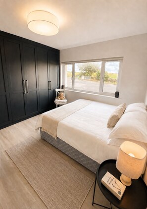 A bedroom with a large bed, a nightstand, a window, and dark wooden wardrobes.