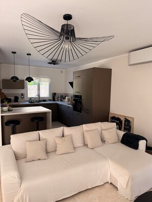 Eine moderne Küche mit einer zentralen Kochinsel, Pendelleuchten und einem Sofa im Wohnbereich.
