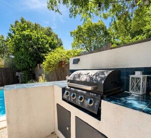 An outdoor grill with a built-in water feature and a pool in the background. - Bright, air-conditioned house in Aix-en-Provence (Aix-en-Provence)