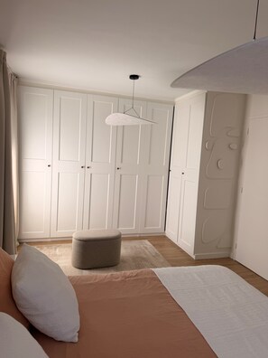 Ein Schlafzimmer mit einem Bett, einer Pendelleuchte, einem Kleiderschrank und einem kleinen Hocker.