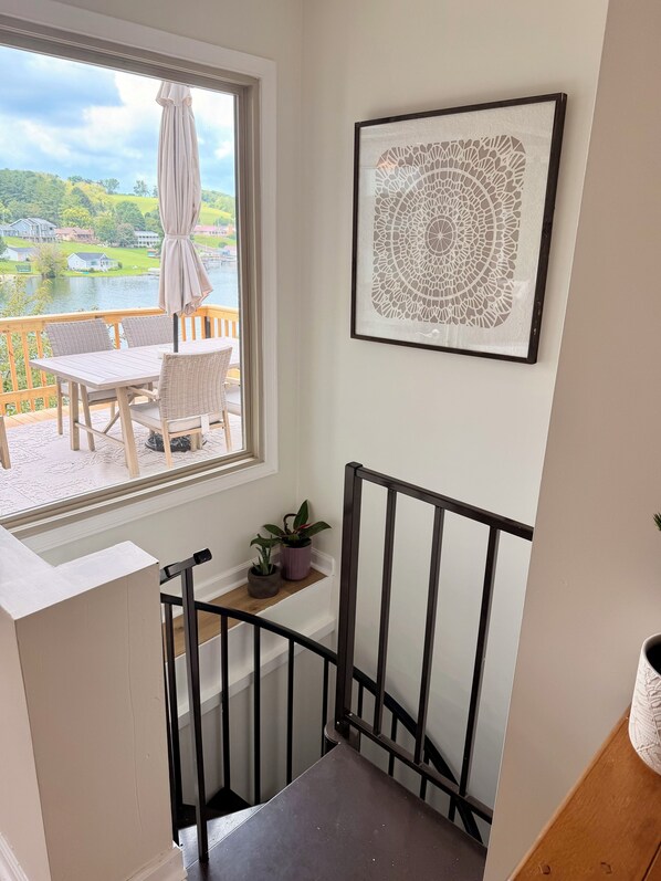 A balcony with a table and chairs, a view of a lake, and a framed artwork on the wall.