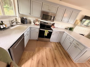 A modern kitchen with grey cabinets, stainless steel appliances, and a wooden floor.
