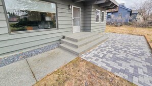 Ein modernes, zweistöckiges Haus mit Veranda, einem kleinen Vorgarten und einem gepflasterten Weg sowie einem Briefkasten.