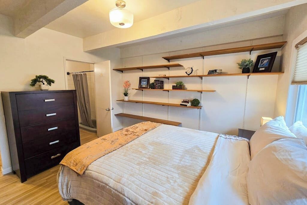 A bedroom with a bed, a dresser, and built-in shelving with decorative items.
