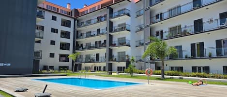 A multi-story residential building with balconies, a swimming pool, and a landscaped garden area.