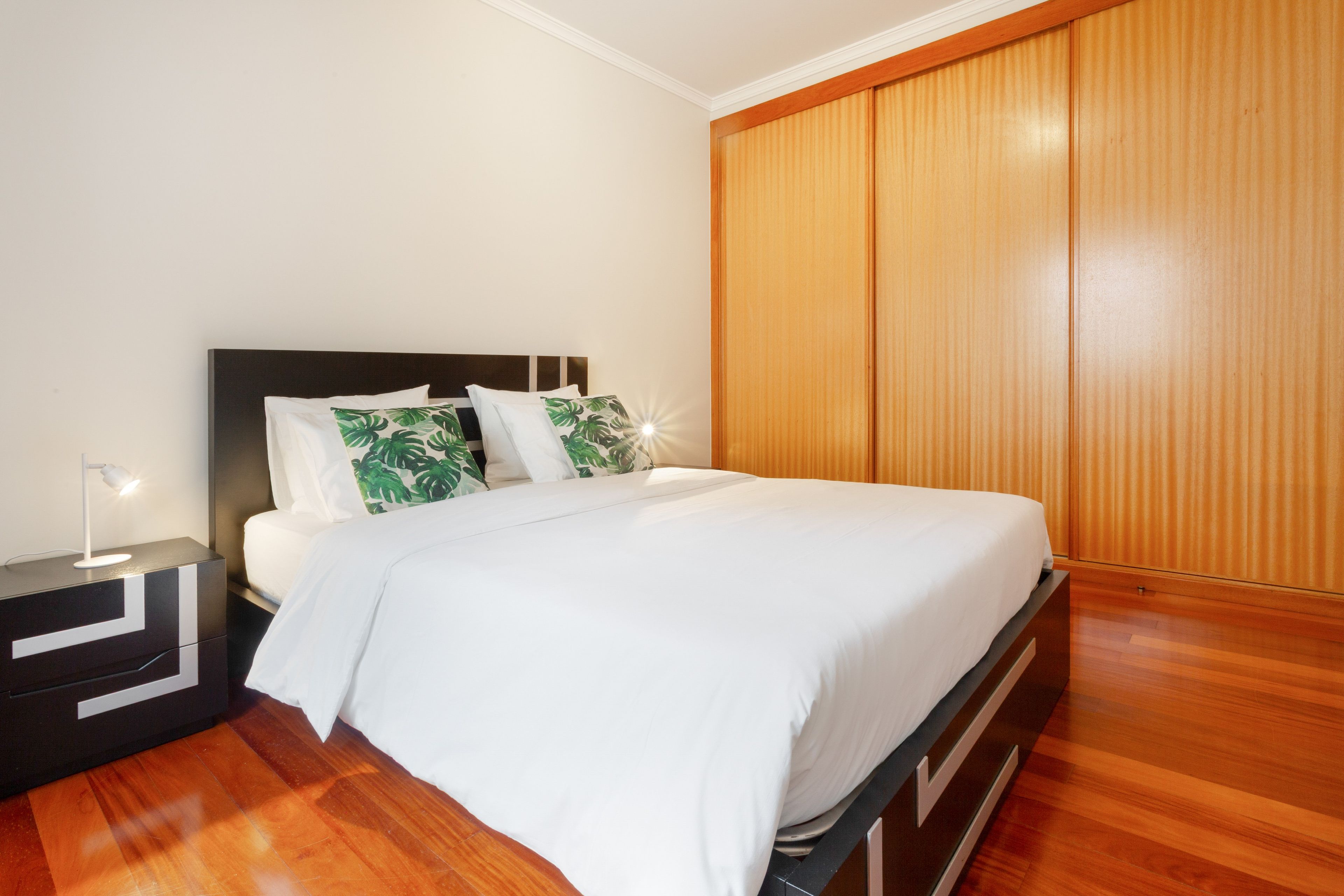 A neatly made bed with white bedding, a bedside lamp, and a nightstand with a modern design.