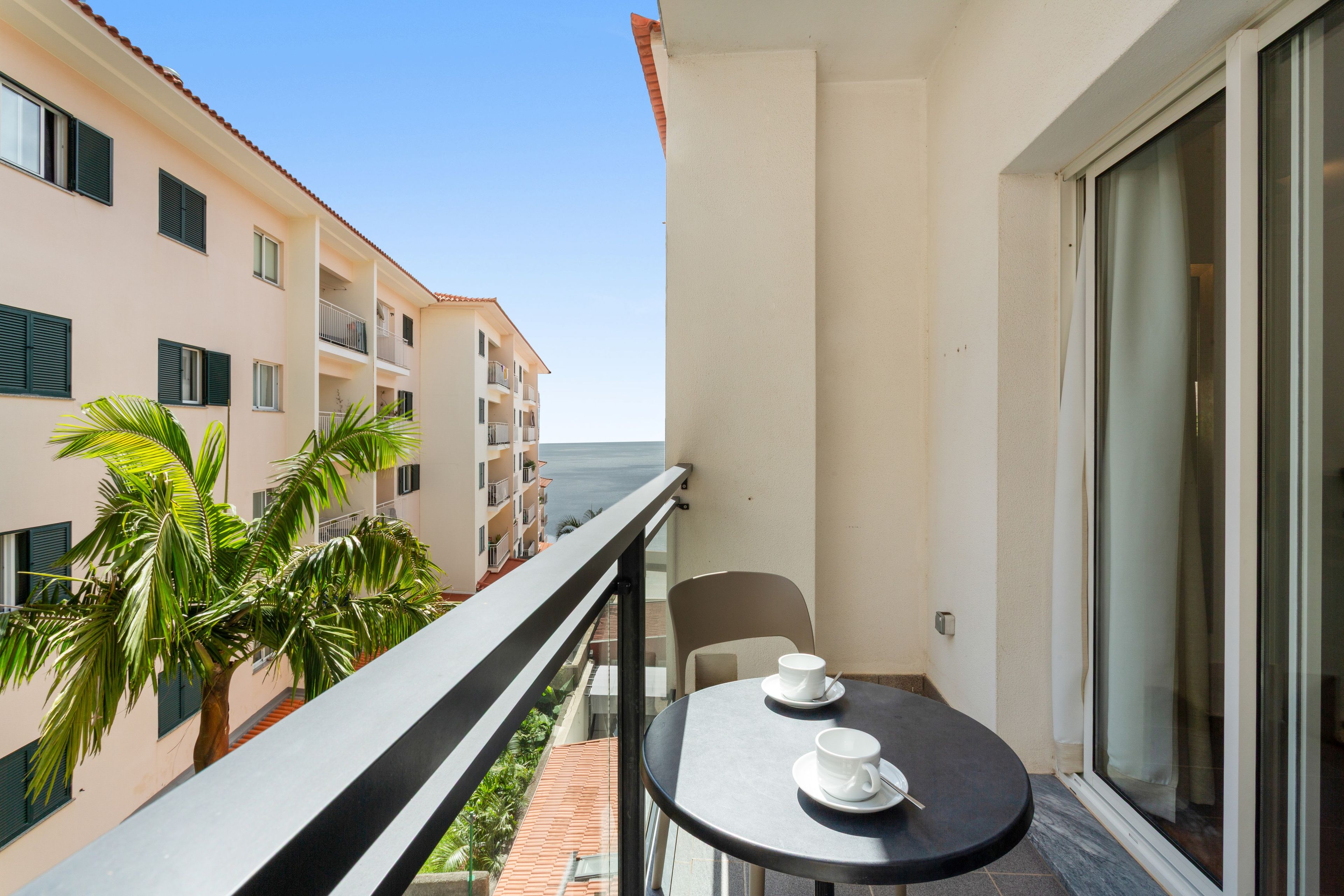 Un balcone con tavolo e sedie, affaccia su un edificio con diversi balconi e una palma.