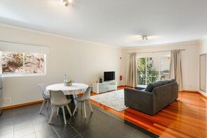 Un salon moderne comprenant un coin repas, un canapé gris, un téléviseur à écran plat et une grande fenêtre donnant sur un paysage verdoyant.