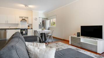 Een moderne woonruimte met een grijze bank, een flatscreen televisie en een eethoek met een tafel en stoelen.