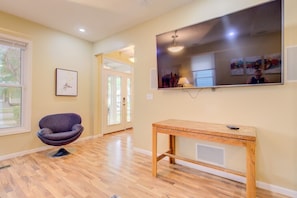 A room with a large flat-screen TV mounted on the wall, a wooden table, a cushioned chair, and a framed picture on the wall. - Spacious Home, Dual King Suites, Central Manhattan (Manhattan)