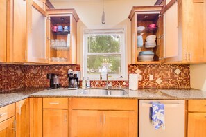 A kitchen with wooden cabinets, a coffee maker, a sink, and a window with a view of trees. - Spacious Home, Dual King Suites, Central Manhattan (Manhattan)