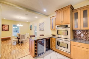 A kitchen with wooden cabinets, a built-in oven, a microwave, and a dining area with a bench and chairs. - Spacious Home, Dual King Suites, Central Manhattan (Manhattan)
