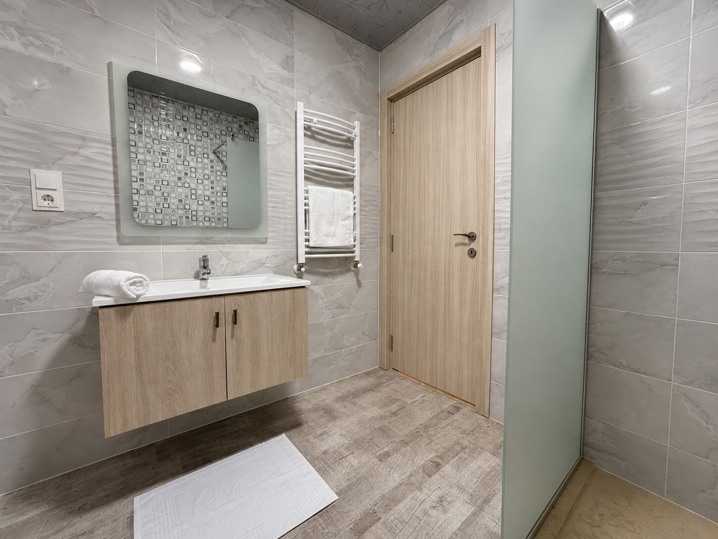 A bathroom with a marble wall, a wooden vanity with a sink, a towel, and a door.