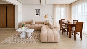 A modern living room with a sectional sofa, a dining table with chairs, a floor lamp, and a patterned rug.
