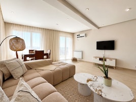 Una sala moderna con un sofá seccional, una mesa de centro, un televisor y un comedor.