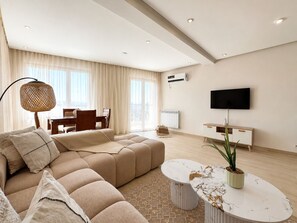 A modern living room with a sectional sofa, a coffee table, a TV, and a dining area. - Superbe 3 pièces a Constantine (El Khroub)