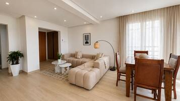Un salon moderne avec un canapé d’angle, une table à manger avec des chaises, une lampe sur pied et une plante en pot.