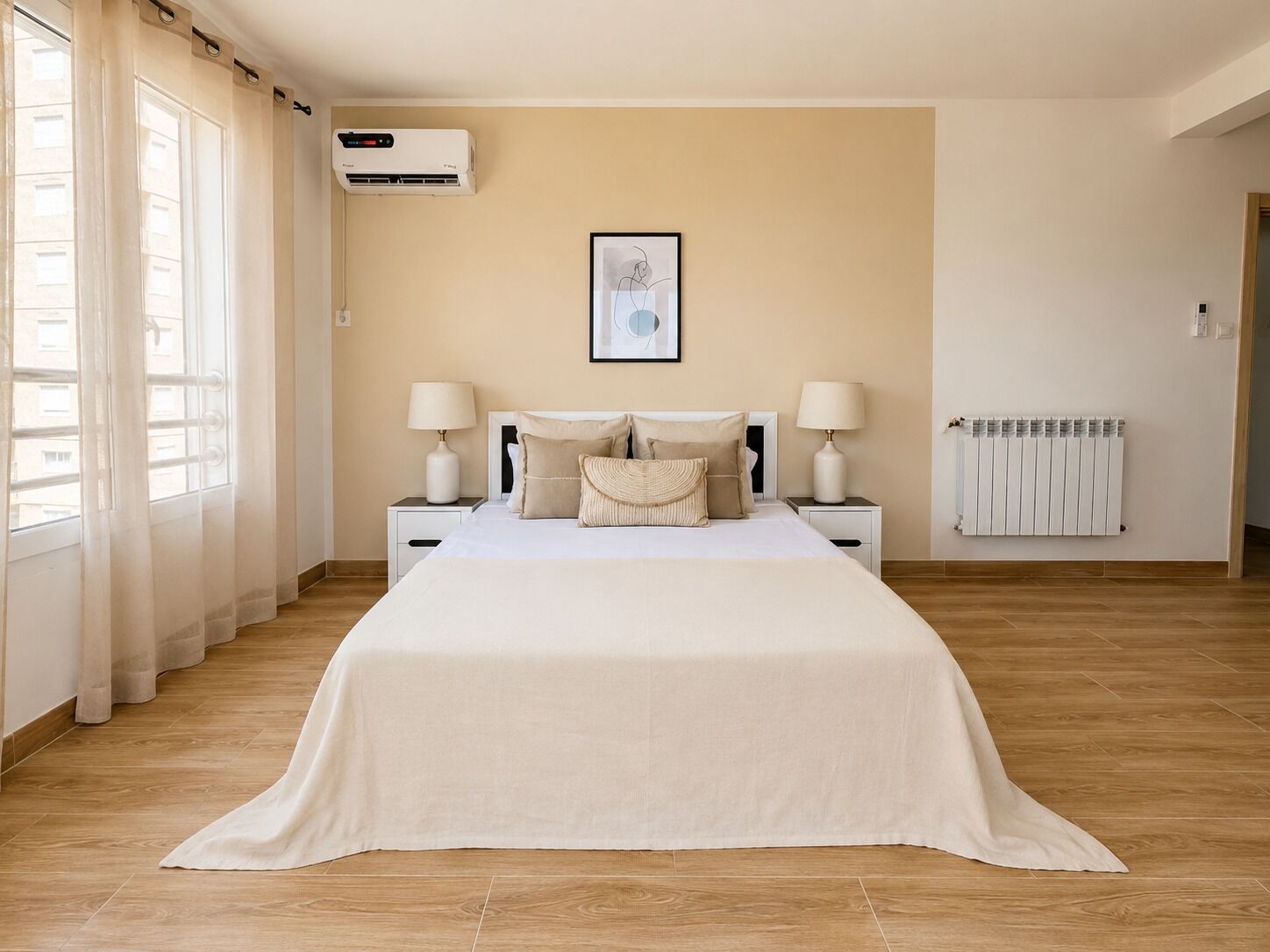 Une chambre à coucher avec un lit, deux tables de chevet avec des lampes, un climatiseur fixé au mur, un tableau encadré et un radiateur.