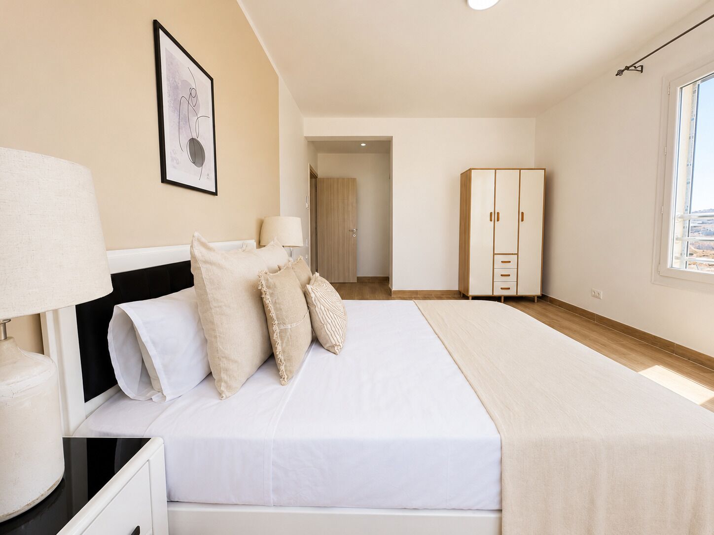 Een slaapkamer met een bed, nachtlampen, een kledingkast en een deur naar een andere kamer.