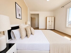 A bedroom with a bed, bedside lamps, a wardrobe, and a door leading to another room.