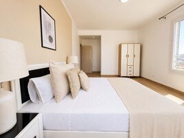 Un dormitorio con cama, lámparas de noche, armario y una puerta que da a otra habitación.