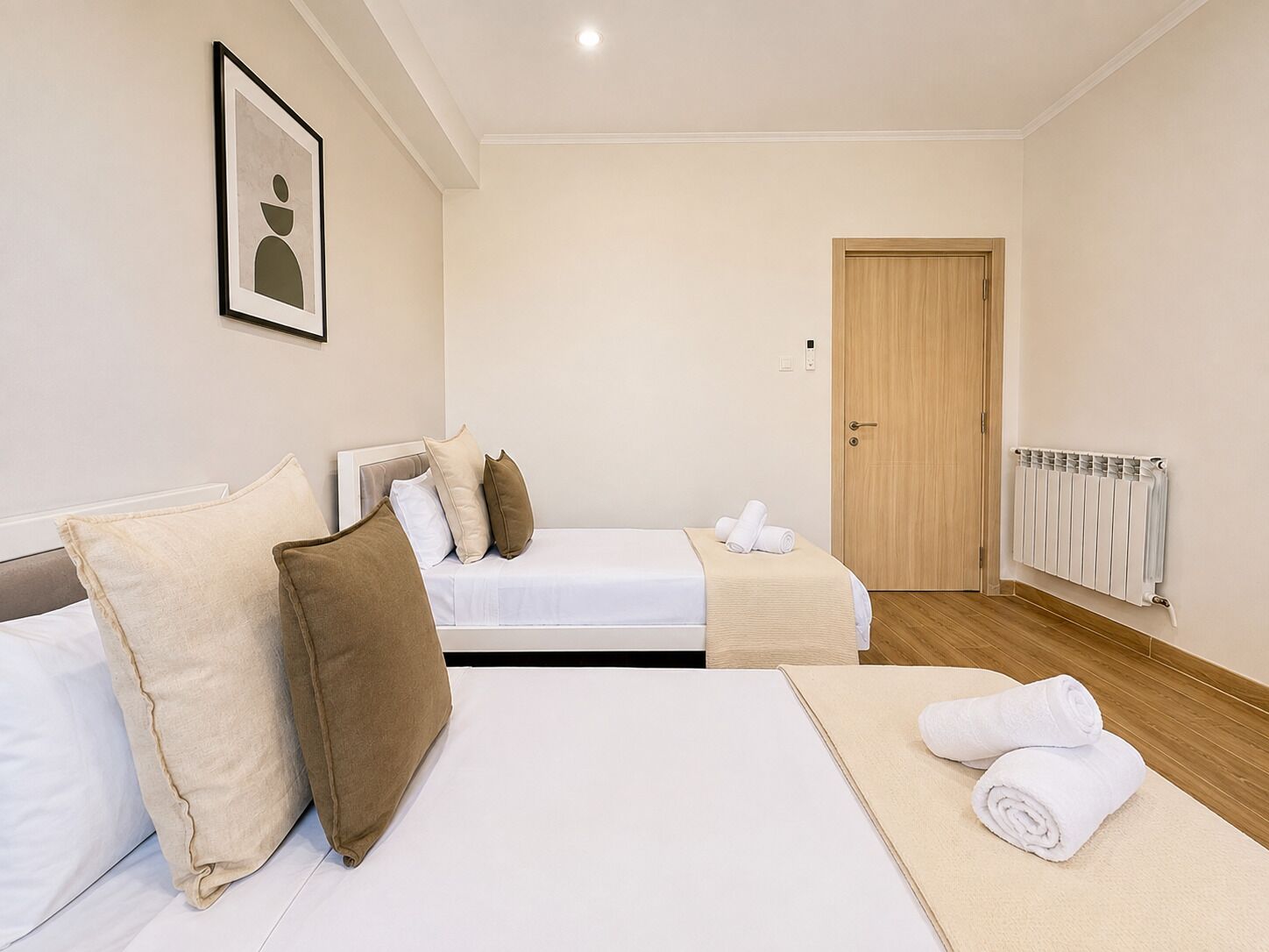 Een hotelkamer met twee bedden, een houten deur, een radiator en een lijst met een afbeelding aan de muur.