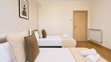 Een hotelkamer met twee bedden, een houten deur, een radiator en een lijst met een afbeelding aan de muur.