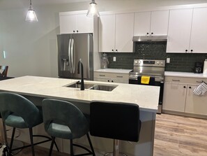 A modern kitchen with a central island, stainless steel appliances, and bar stools.