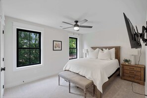 Ein Schlafzimmer mit einem Bett, einer Sitzbank, einem Nachttisch, einem an der Wand montierten Fernseher und einem Deckenventilator.